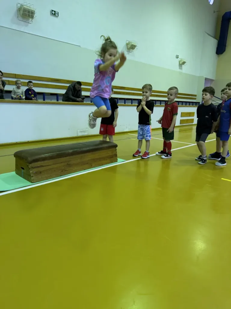 Dziewczynka zeskakuje z ławeczki gimnastycznej na zajęciach Rozrabiaków