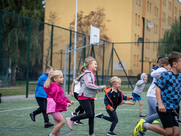 Grupa dzieci biegnie na boisku podczas treningu