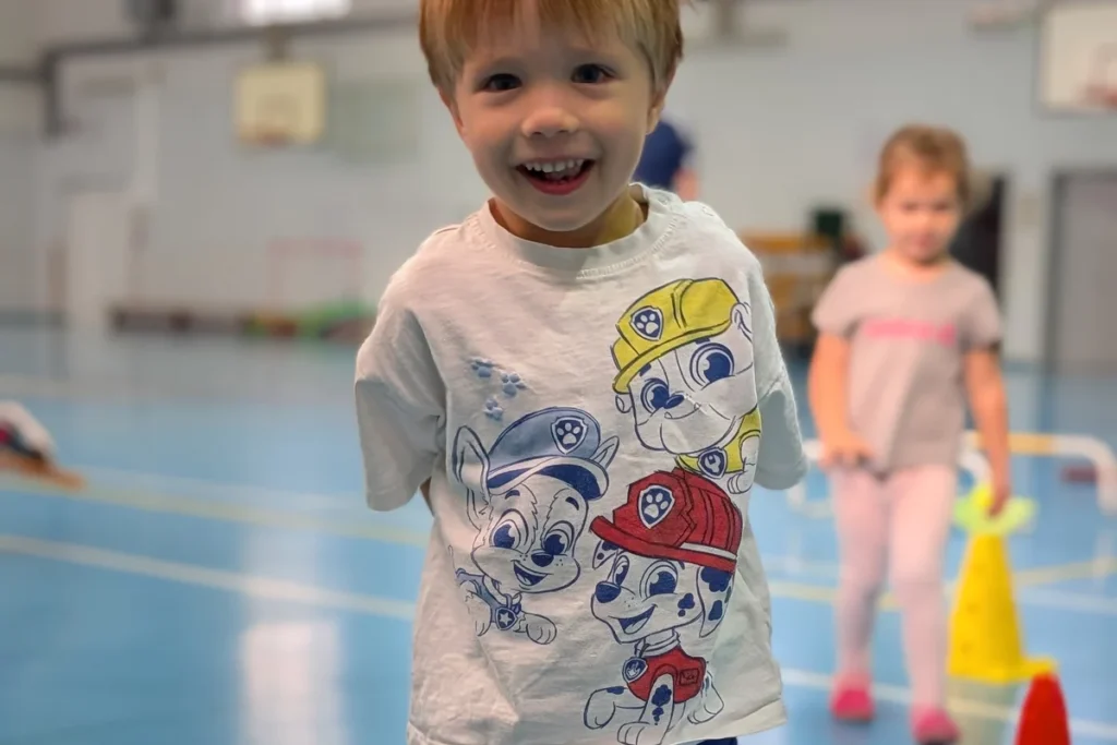 Uśmiechnięty kilkuletni chłopiec na zajęciach sportowych w sali gimnastycznej