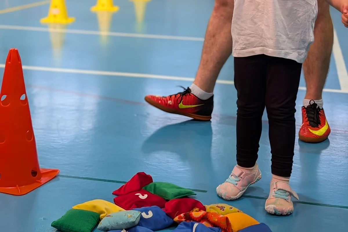 Buty sportowe dzieci na podłodze sali gimnastycznej obok kolorowych woreczków