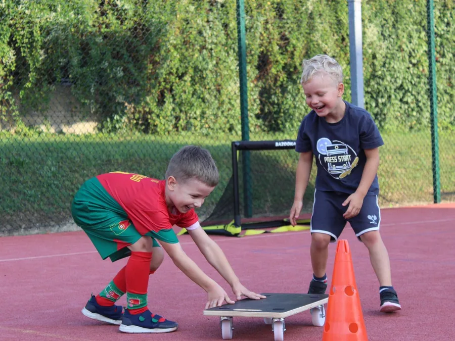 Dwaj roześmiani chłopcy przy desce równoważnej na boisku